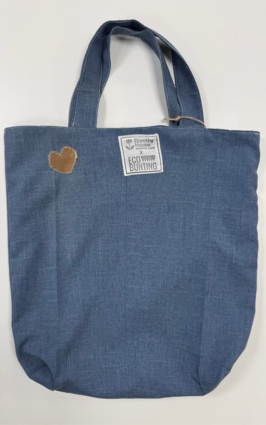 Blue tote bag with a heart patch and label on a white background