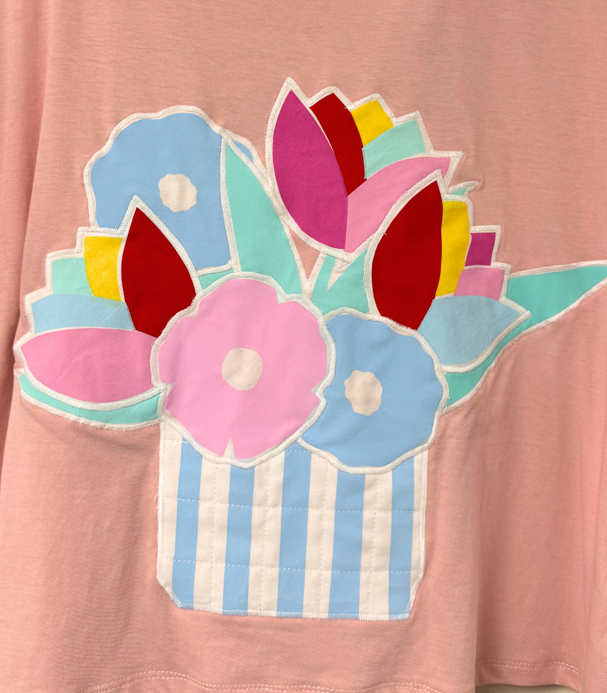 Pink shirt with colorful flower design on a plain background