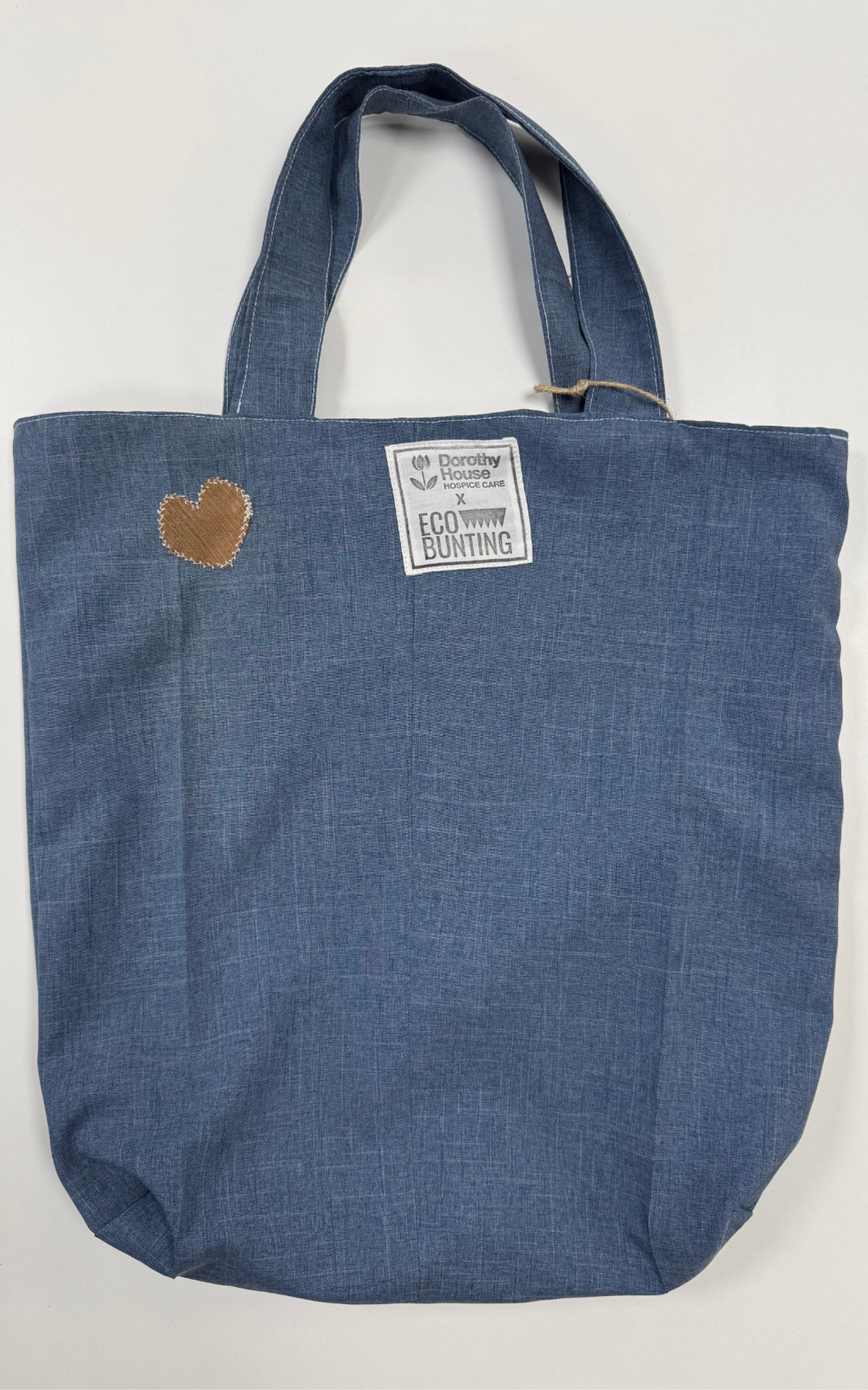 Blue tote bag with a heart patch and label on a white background