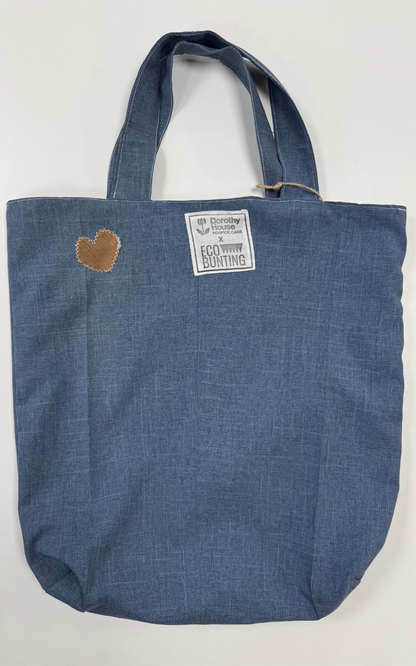 Blue tote bag with a heart patch and label on a white background