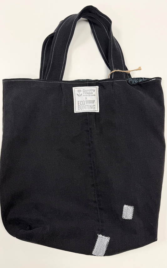 Black tote bag with a visible brand label on a beige background